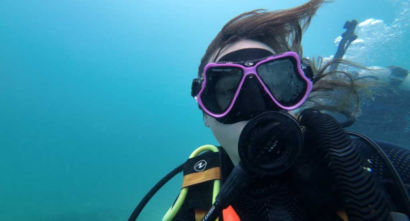 A person looks into the camera while scuba diving